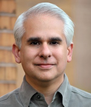 Arthur Rishi, Co-Executive Director Headshot. He is smiling, a brick wall is behind him.