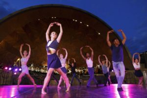 Dancers from Landmarks Dance Night perform onstage at the Hatch Shell. Purple lights illuminate them as the Hatch Shell stands behind them.