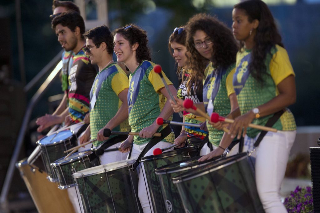Performers from Cirandadas by Clarice Assad stand, smiling and holding their drums for the piece.