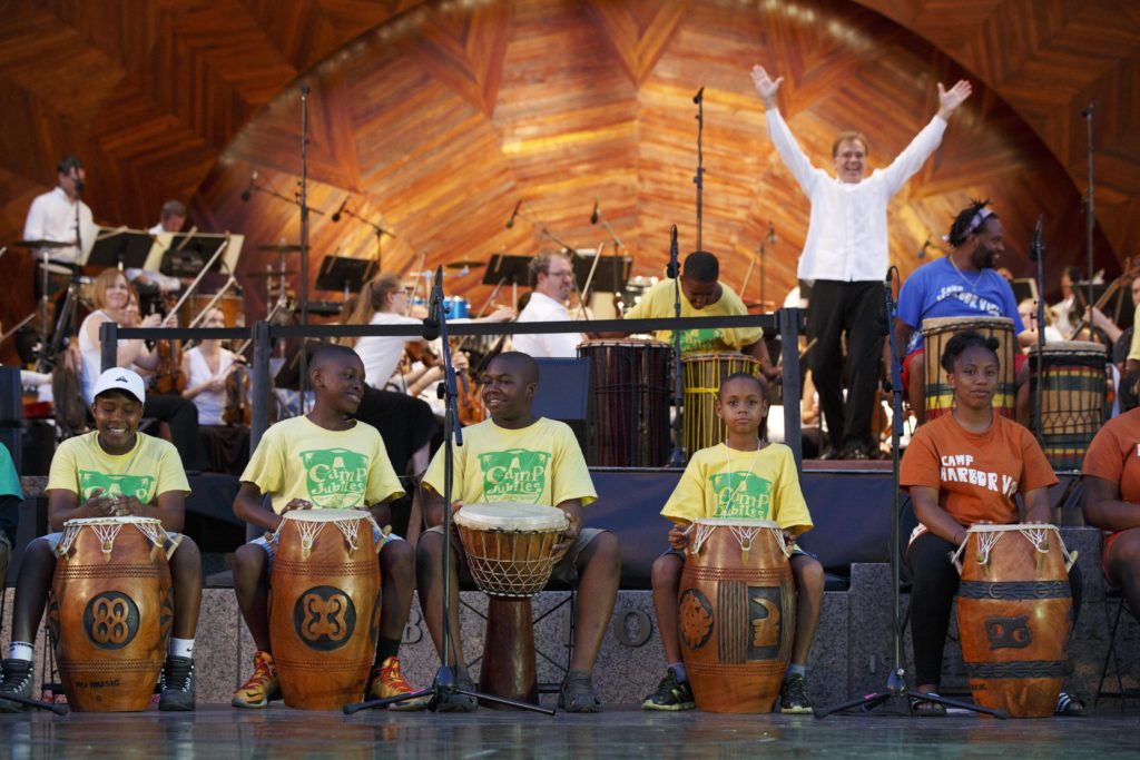 Musicians have drums in front of them for 2016 Hermana Frontera (Sister Border) by Gonzalo Grau and Maestro, Christopher Wilkins stands with his hands up in the air.