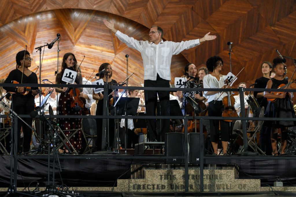 Maestro, Christopher Wilkins, holds his hands out as Landmarks Orchestra musicians convene behind him.