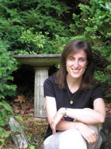 Francine Trester is sitting, smiling at the camera. She is outside, surrounded by greenery. 