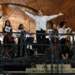 Maestro Christopher Wilkins stands with his arms open wide, as the Landmarks Orchestra plays.
