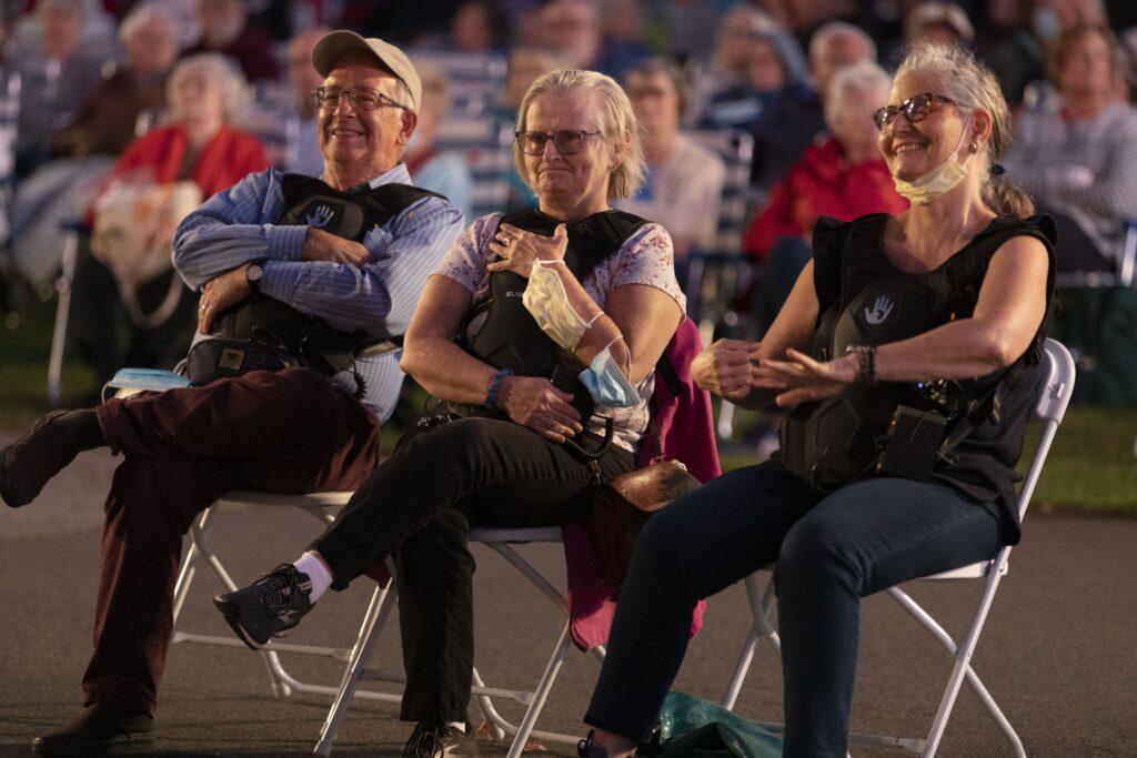 Audience members who are Deaf are wearing Subpacs, smiling and watching Landmarks Orchestra perform.