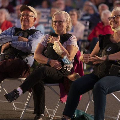 Audience members who are Deaf are wearing Subpacs, smiling and watching Landmarks Orchestra perform.