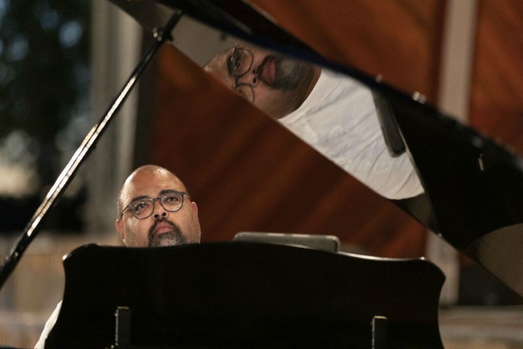 David Coleman sitting by a grand piano, looking up.