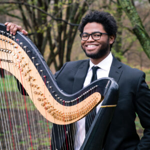 Charles Overton smiles and stands next to his harp.
