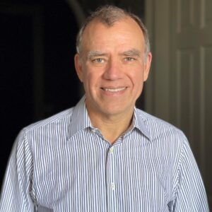 Christopher Wilkins, smiles. He is wearing a light blue shirt.