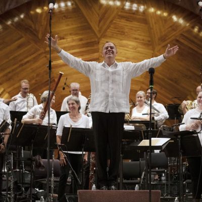 Music Director, Christopher Wilkins is about to take a bow, has his hands extended and is smiling.