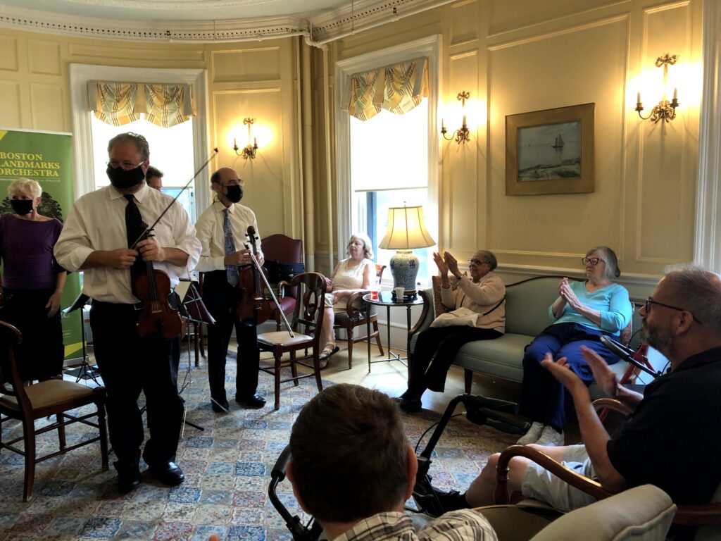 Musicians from Landmarks Orchestra stand as residents that make up the audience applaud.