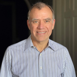 Headshot of Christopher Wilkins. He is smiling, wearing a gray and light blue shirt.