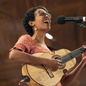 Fabiola Méndez plays her cuatro, singing into a microphone.