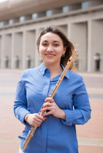 Headshot of Anabel Gil Diaz. She is wearing a blue, button-down shirt, holding a flute, standing outside.