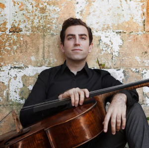 Headshot of Tommy Mesa - he's sitting against a brick wall, holding his cello.