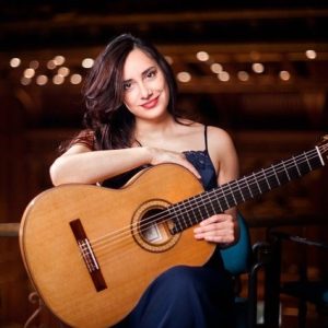 Zaira Meneses holds a guitar, smiling.