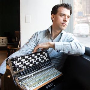 Headshot of Julien Labro. He is looking out of a window, holding an accordion.